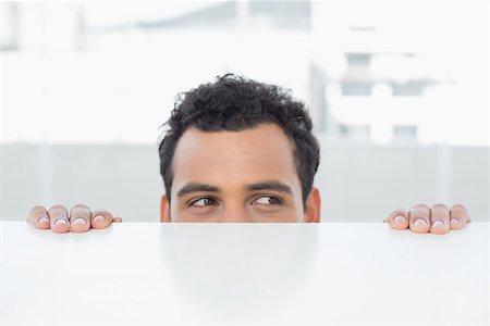 Close-up of a young businessman peeking behind the desk at bright office Stock Photo - Budget Royalty-Free & Subscription, Code: 400-07228527