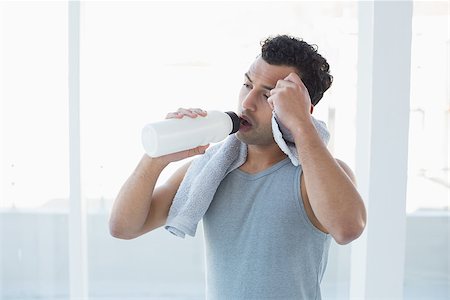 simsearch:400-05115517,k - Tired young man drinking water while wiping sweat with towel in a bright fitness studio Stock Photo - Budget Royalty-Free & Subscription, Code: 400-07228719