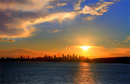 The sun setting over beautiful Sydney Harbour, its golden orange rays bouncing off the underside of the clouds, and that's  Sydney City in distance as a silhouette.  Ahh summer in the city. Stock Photo - Budget Royalty-Free & Subscription, Code: 400-07223786