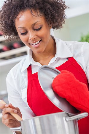 A beautiful mixed race African American girl or young woman looking happy wearing red apron & cooking in her kitchen at home Stock Photo - Budget Royalty-Free & Subscription, Code: 400-07264827