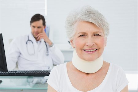 Senior patient in surgical collar with male doctor sitting at desk in background at medical office Stock Photo - Budget Royalty-Free & Subscription, Code: 400-07267801