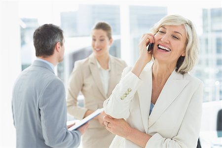 simsearch:6108-06907863,k - Smiling mature businesswoman on call with colleagues discussing in background at a bright office Stock Photo - Budget Royalty-Free & Subscription, Code: 400-07274479