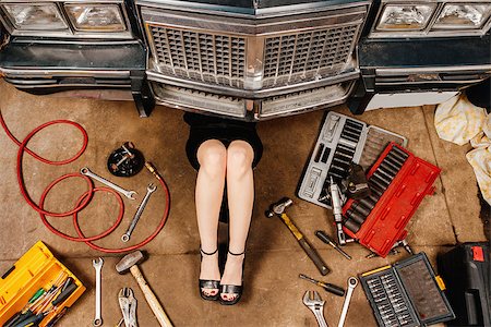 A woman wearing a black skirt and heels doing repairs under the front of an old car from the early 80's. Stock Photo - Budget Royalty-Free & Subscription, Code: 400-07294073