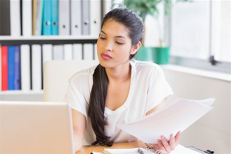 Young businesswoman holding papers while looking at laptop in office Stock Photo - Budget Royalty-Free & Subscription, Code: 400-07334227