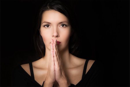 Dark evocative portrait of a spiritual young woman praying with her hands clasped and an intent look in her eyes Stock Photo - Budget Royalty-Free & Subscription, Code: 400-07331420