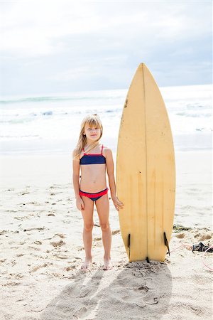 Cute young girl standing next to surfboard on beach with ocean in background Stock Photo - Budget Royalty-Free & Subscription, Code: 400-07420198