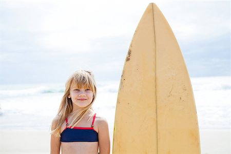 Happy smiling cute young girl standing next to surfboard on beach with sky and ocean in background Stock Photo - Budget Royalty-Free & Subscription, Code: 400-07420199