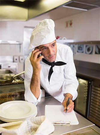 Concentrated male cook writing on clipboard while using cellphone in the kitchen Stock Photo - Budget Royalty-Free & Subscription, Code: 400-07468076