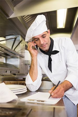 Concentrated male cook writing on clipboard while using cellphone in the kitchen Stock Photo - Budget Royalty-Free & Subscription, Code: 400-07468071