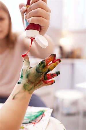 Young child playing with finger paints holding out its hand as the mother applies bright orange paint from a tube Stock Photo - Budget Royalty-Free & Subscription, Code: 400-07479508