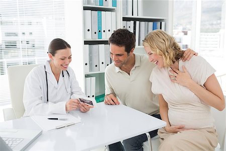 Happy female gynaecologist and expectant couple looking at sonography reports in clinic Photographie de stock - Aubaine LD & Abonnement, Code: 400-07473283