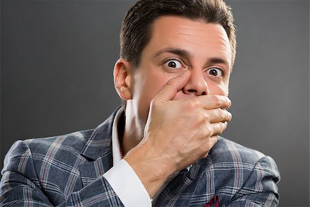 simsearch:400-04175955,k - Portrait of afraid businessman wearing suit covering his mouth with his hand over grey background. Stock Photo - Budget Royalty-Free & Subscription, Code: 400-07568083