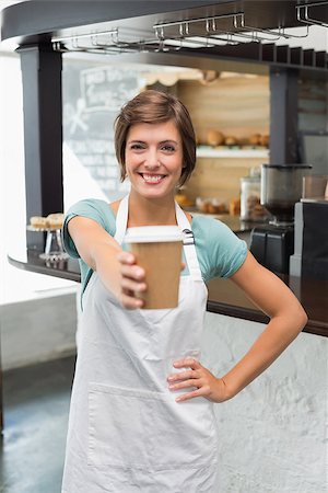 simsearch:400-07750853,k - Pretty barista smiling at camera holding disposable cup at the coffee shop Stock Photo - Budget Royalty-Free & Subscription, Code: 400-07750845