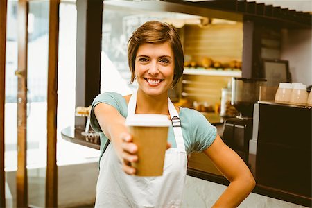 simsearch:400-07750853,k - Pretty barista smiling at camera holding disposable cup at the coffee shop Stock Photo - Budget Royalty-Free & Subscription, Code: 400-07750846