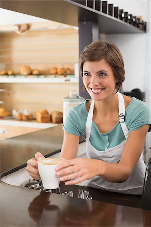 simsearch:400-07750853,k - Pretty barista offering cup of coffee smiling at the coffee shop Stock Photo - Budget Royalty-Free & Subscription, Code: 400-07750854
