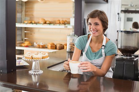 simsearch:400-07750853,k - Pretty barista offering cup of coffee smiling at the coffee shop Stock Photo - Budget Royalty-Free & Subscription, Code: 400-07750855