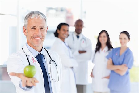 Mature doctor holding an apple wearing breast cancer awareness ribbon Stock Photo - Budget Royalty-Free & Subscription, Code: 400-07835176