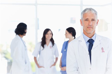 Mature doctor standing in the foreground wearing  breast cancer awareness ribbon Stock Photo - Budget Royalty-Free & Subscription, Code: 400-07835184