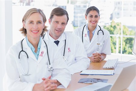 Smiling doctors posing at their desk wearing breast cancer awareness ribbon Stock Photo - Budget Royalty-Free & Subscription, Code: 400-07835182