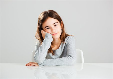 Beautiful little girl sitting behind a desk with a distracted expression, against a gray background Stock Photo - Budget Royalty-Free & Subscription, Code: 400-07897688