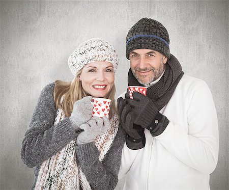 simsearch:400-07957420,k - Happy couple in winter fashion holding mugs against weathered surface Photographie de stock - Aubaine LD & Abonnement, Code: 400-07957424
