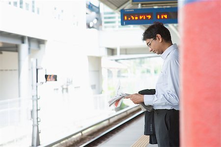 Candid Asian Indian businessman waiting at public train station, standing and reading on newspaper. Stock Photo - Budget Royalty-Free & Subscription, Code: 400-07978352