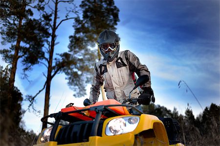 Horizontal close-up of a man in helmet and safety goggles looking into the camera while sitting on quad bike against vivid blue sky. Stock Photo - Budget Royalty-Free & Subscription, Code: 400-07993447