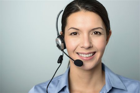 Attractive female call center operator, client services assistant or telemarketer wearing a headset looking at the camera with a charming friendly smile, on grey with copy space Stock Photo - Budget Royalty-Free & Subscription, Code: 400-07993945