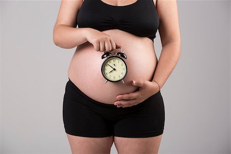 simsearch:400-04396054,k - Pregnant woman showing her belly with a clock, over a gray background Stock Photo - Budget Royalty-Free & Subscription, Code: 400-08070631