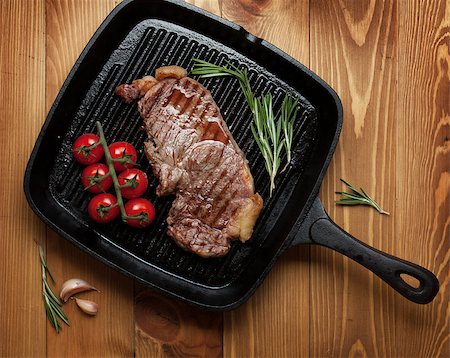 Sirloin steak with rosemary and cherry tomatoes on frying pan over wooden table Stock Photo - Budget Royalty-Free & Subscription, Code: 400-08072738