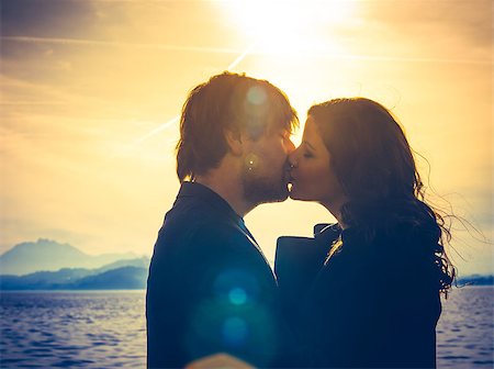 Photo of young adults by the water hugging and kissing in the late afternoon as the sun lowers in the sky. Heavily filtered for more romantic effect. Real lens flare visible. Stock Photo - Budget Royalty-Free & Subscription, Code: 400-08073656