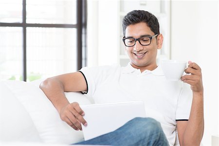 Indian guy enjoying a cup of hot tea while using digital pc tablet at home. Asian man relaxed and sitting on sofa indoor. Handsome male model. Stock Photo - Budget Royalty-Free & Subscription, Code: 400-08114413