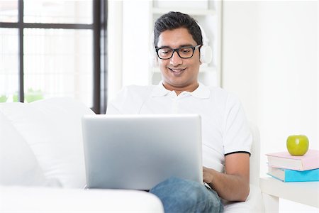 Indian guy listening to music with headset and laptop computer at home. Asian man using internet indoor, relaxed and sitting on sofa. Handsome male model. Stock Photo - Budget Royalty-Free & Subscription, Code: 400-08114421