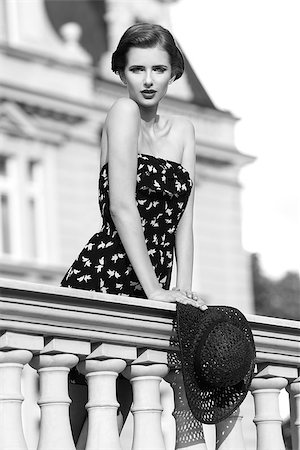 black and white shot ,outside fashion shoot of cute brunette girl with summer elegant style posing on old balcony with short dress and stylish hat in the hand. Looking in camera. Stock Photo - Budget Royalty-Free & Subscription, Code: 400-08116229