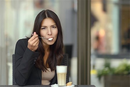 Woman sitting in a coffee house or cafeteria savoring a tasty cup of cappuccino coffee sipping the frothy foam off a spoon while looking at the camera Photographie de stock - Aubaine LD & Abonnement, Code: 400-08160557