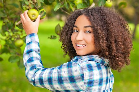 Outdoor portrait of beautiful happy mixed race African American girl teenager female child picking an organic green apple in an orchard and smiling with perfect teeth Stock Photo - Budget Royalty-Free & Subscription, Code: 400-08297652