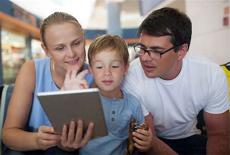 Young parents and little son at the airport. Mother holding pad and boy playing game, both parents looking at screen. Entertaining during flight waiting Stock Photo - Budget Royalty-Free & Subscription, Code: 400-08333311