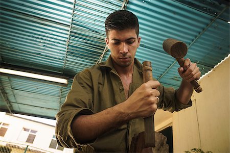 simsearch:400-07899762,k - Young man at work learning craftsman profession, working with hammer and chisel. The artist carves a raw block of wood to make a wooden statue Stock Photo - Budget Royalty-Free & Subscription, Code: 400-08349525