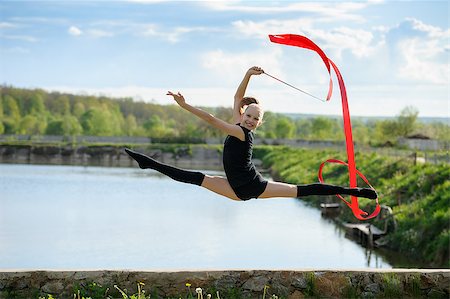 Rhythmic gymnast girl performing with a red ribbon outdoor. Leg-split in a jump against rural nature background Stock Photo - Budget Royalty-Free & Subscription, Code: 400-08370926