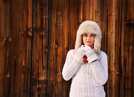 Winter in the country style. Young woman in white knitted sweater and furry hat holding red cup in the front of rustic wood wall Stock Photo - Budget Royalty-Free & Subscription, Code: 400-08414756