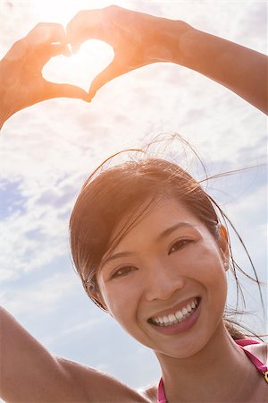simsearch:400-06422339,k - Beautiful young smiling Chinese Asian woman girl on a beach in a bikini, making a hand heart shaped finger frame Foto de stock - Super Valor sin royalties y Suscripción, Código: 400-08433188