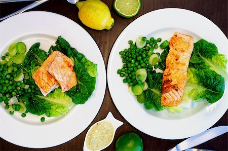 Delicious Roasted Salmon with Sweet Pea, Leek and Salad Romano on White Plates with Lemon and Sauce closeup on Dark Wooden background. Selective Focus Stock Photo - Budget Royalty-Free & Subscription, Code: 400-08574239