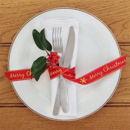 Table setting with white porcelain plate, knife and fork, linen serviette, holly and merry christmas red ribbon over oak background. Stock Photo - Budget Royalty-Free & Subscription, Code: 400-08627886