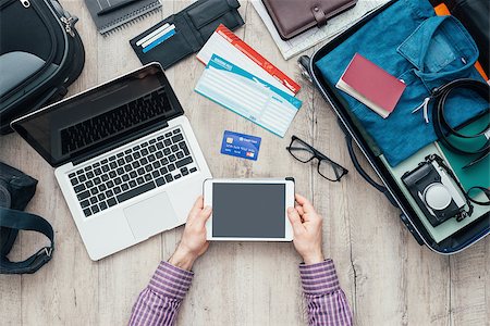 Traveler getting ready for a trip, he is packing his bag and using a digital touch screen tablet, flat lay Stock Photo - Budget Royalty-Free & Subscription, Code: 400-08751432
