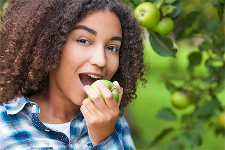 Outdoor portrait of beautiful happy mixed race African American girl teenager female child eating an organic green apple and smiling with perfect teeth Stock Photo - Budget Royalty-Free & Subscription, Code: 400-08774469