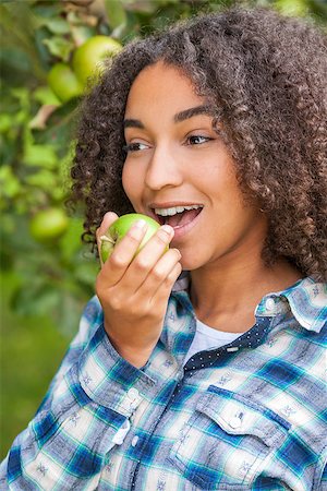 Outdoor portrait of beautiful happy mixed race African American girl teenager female child eating an organic green apple and smiling with perfect teeth Photographie de stock - Aubaine LD & Abonnement, Code: 400-08773125