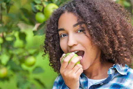 Outdoor portrait of beautiful happy mixed race African American girl teenager female child eating an organic green apple and smiling with perfect teeth Photographie de stock - Aubaine LD & Abonnement, Code: 400-08773126