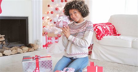 sweater and fireplace - Pretty happy young woman checking her Christmas gifts on the floor in her living room holding up a decorative box tied with a bow with friendly smile. Stock Photo - Budget Royalty-Free & Subscription, Code: 400-08811115