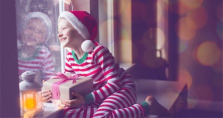 santa children - panorama of happy smiling boy holding nicely wrapped gift sitting cozy at home looking out the window while snowing waiting for christmas miracle, christmas lights and decorations, holiday concept, toned image Stock Photo - Budget Royalty-Free & Subscription, Code: 400-08888145