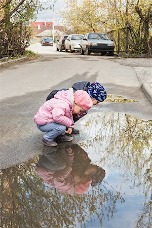 Two children sit on the asphalt road and look at their reflection in a puddle Stock Photo - Budget Royalty-Free & Subscription, Code: 400-08961382